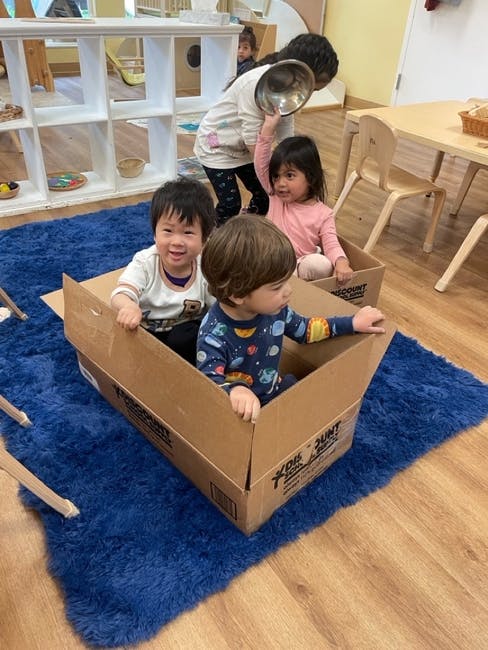 Three children playing in cardboard boxes on a blue rug