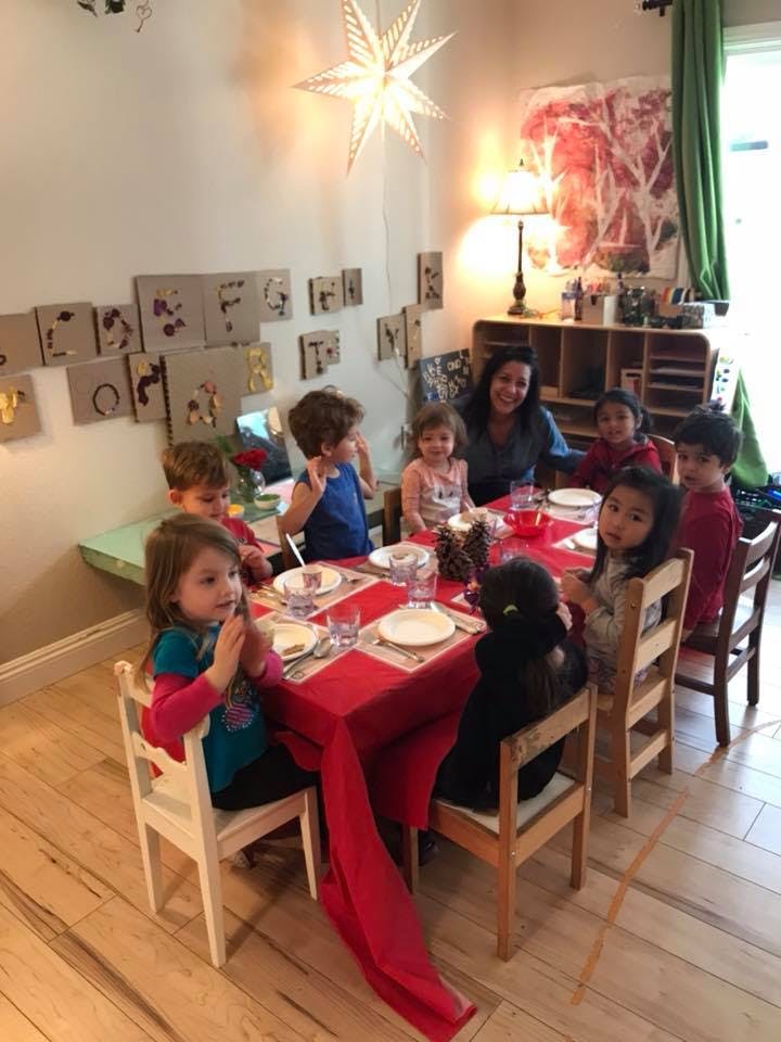 Adult and children sitting around a table set with red tablecloth and plates