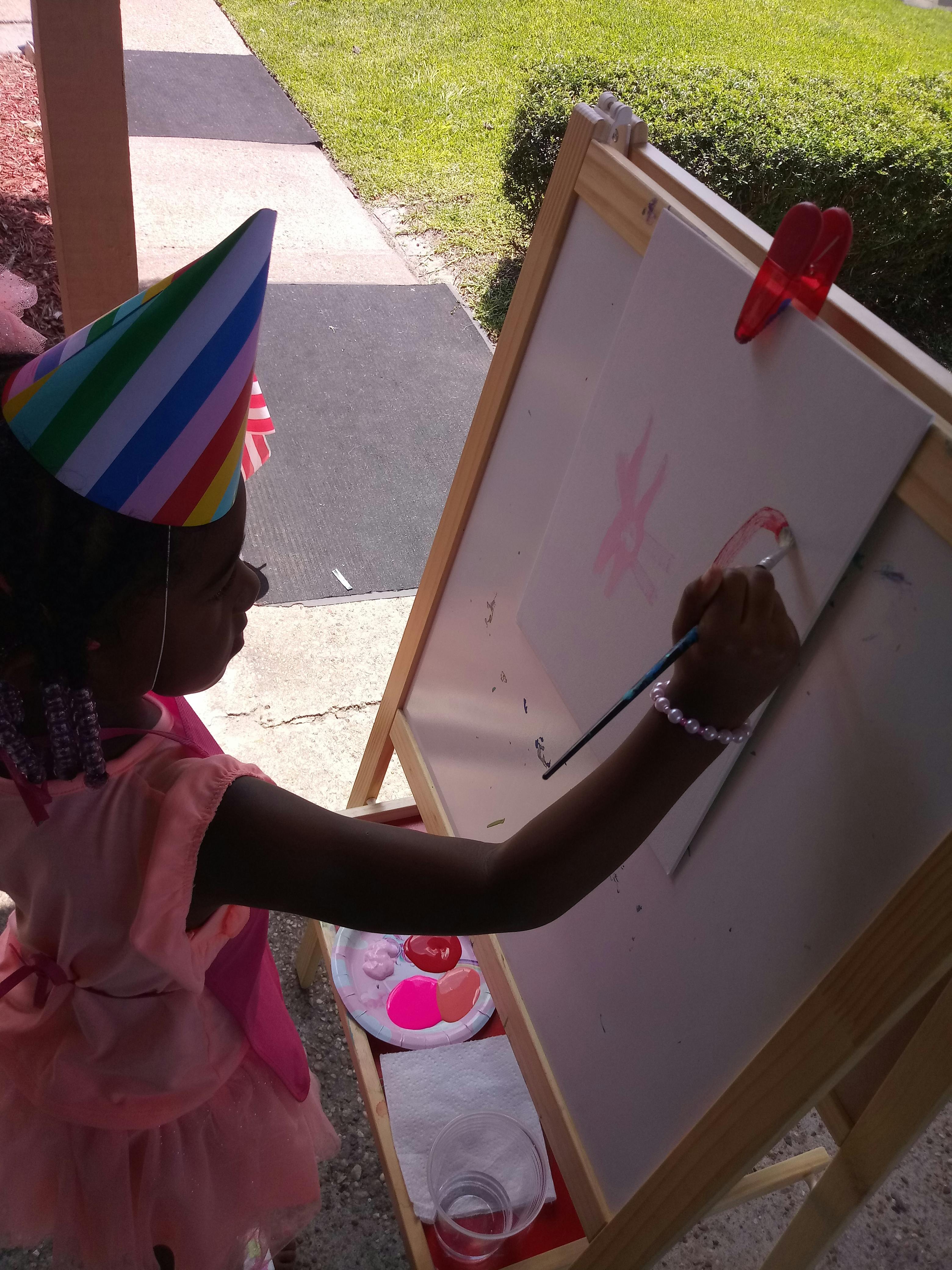 Child in a party hat painting on an easel