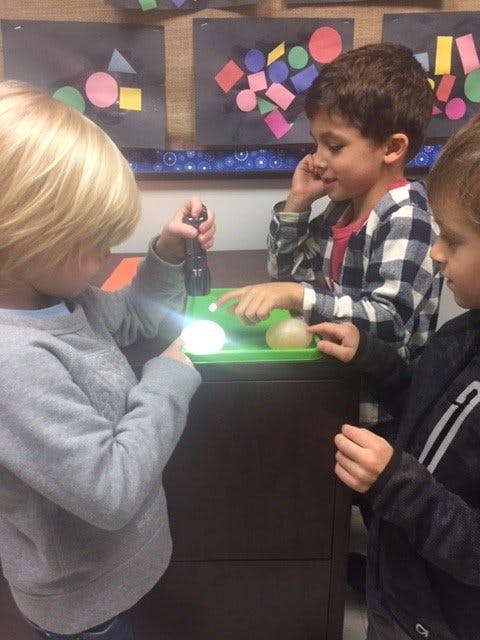 Three children looking at a flashlight and glowing objects