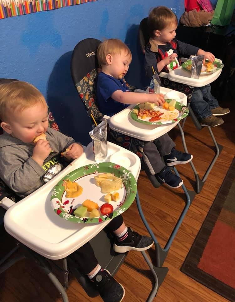 Three children sitting in high chairs eating food from plates