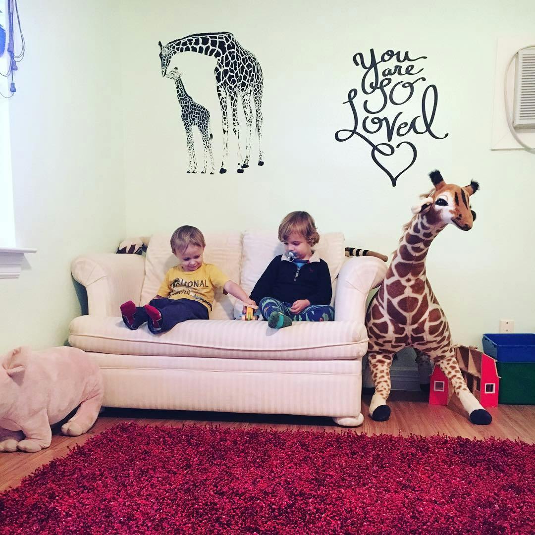 Two children sitting on a couch with a large stuffed giraffe