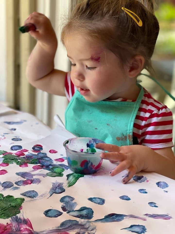 Child painting on paper with fingers and a crayon