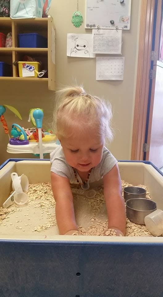Child playing in a sensory bin with oats