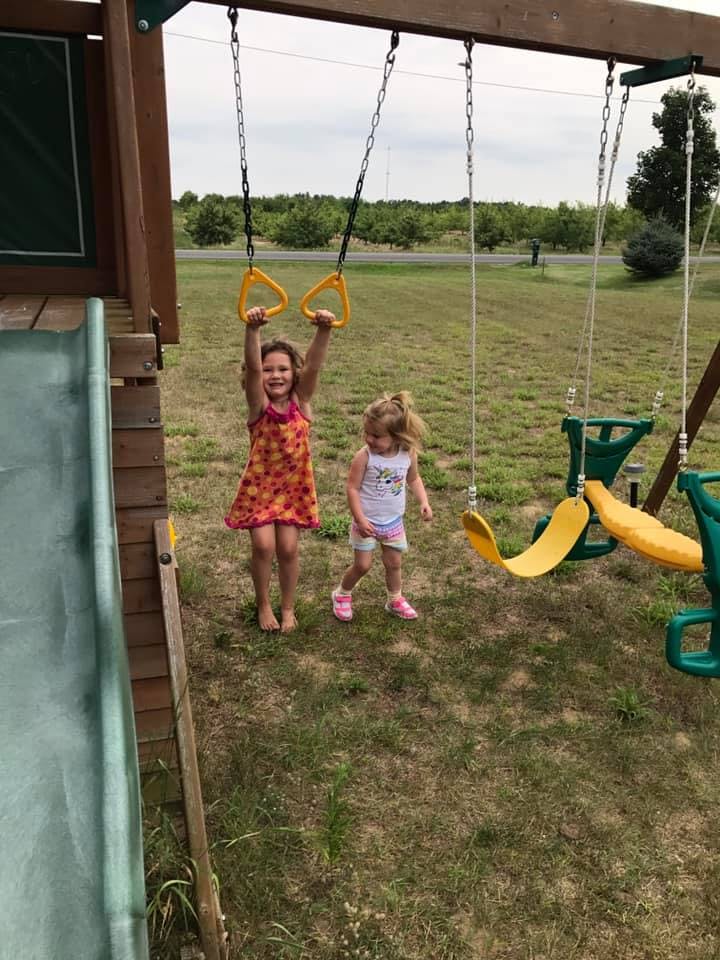 Child holding onto monkey rings on a playground with another child nearby