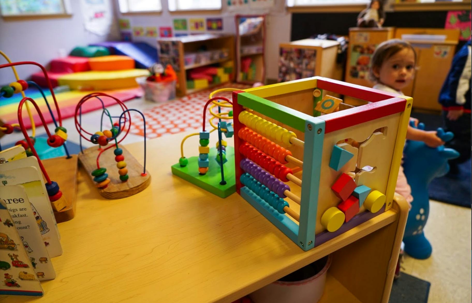 Child standing next to a wooden activity cube with beads and shapes