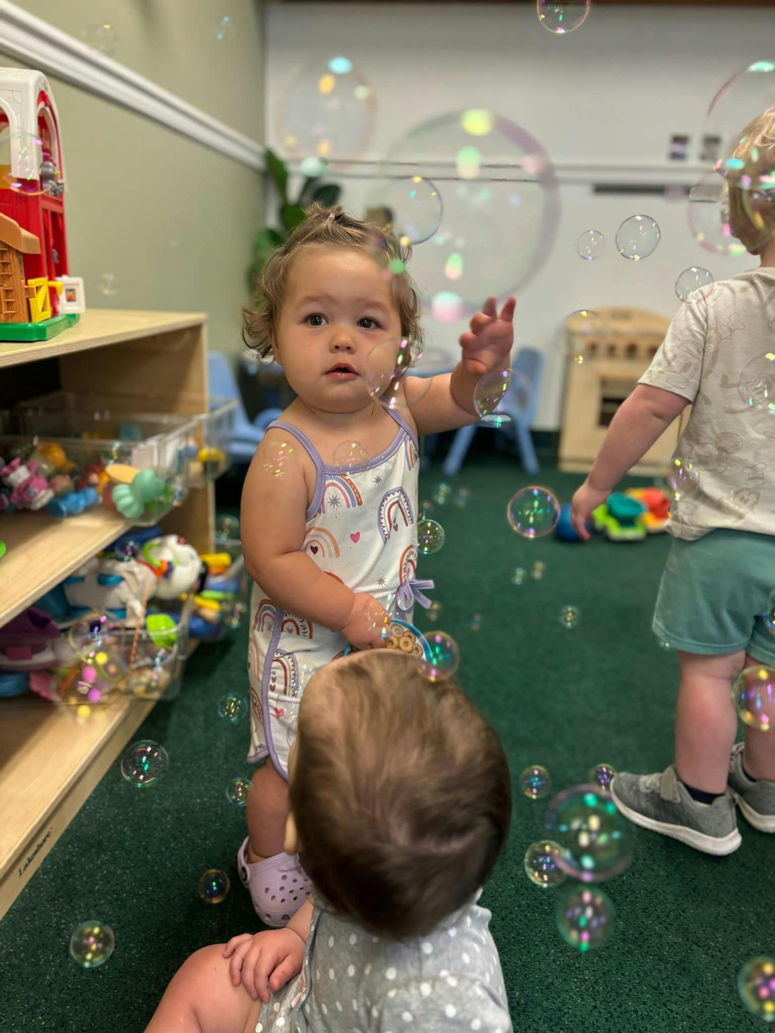 Child reaching for bubbles in a room with other children