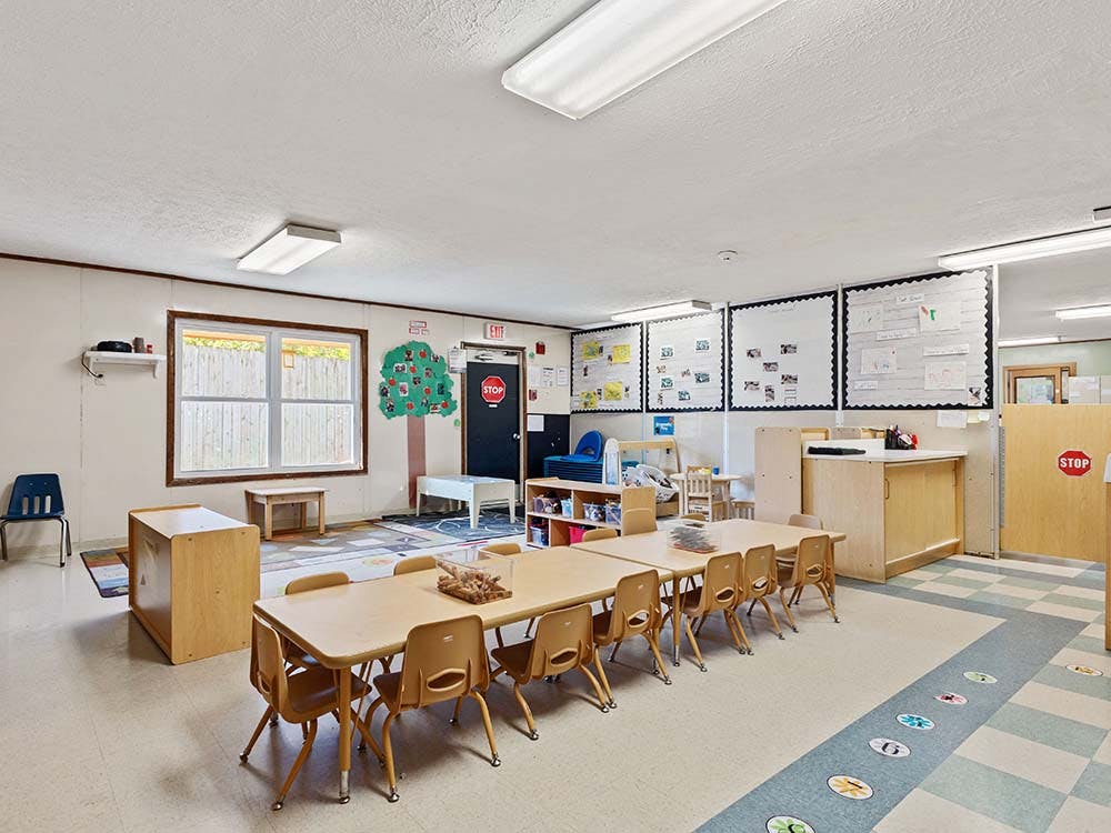 Empty preschool classroom with small tables and chairs, whiteboards on the walls