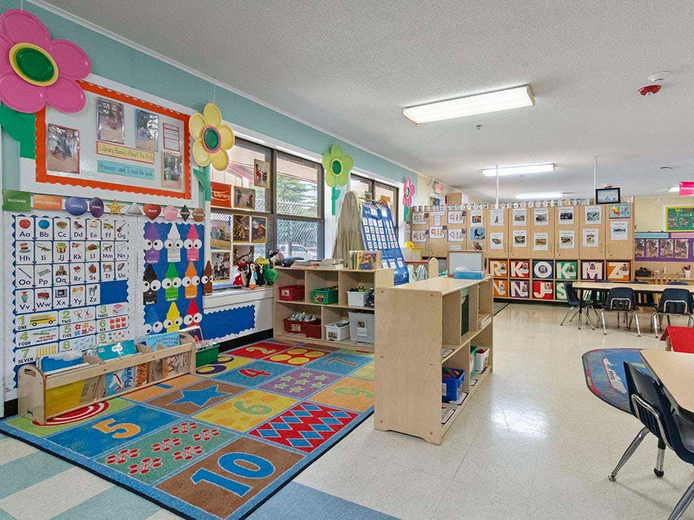 A colorful empty classroom with an alphabet rug and small tables and chairs