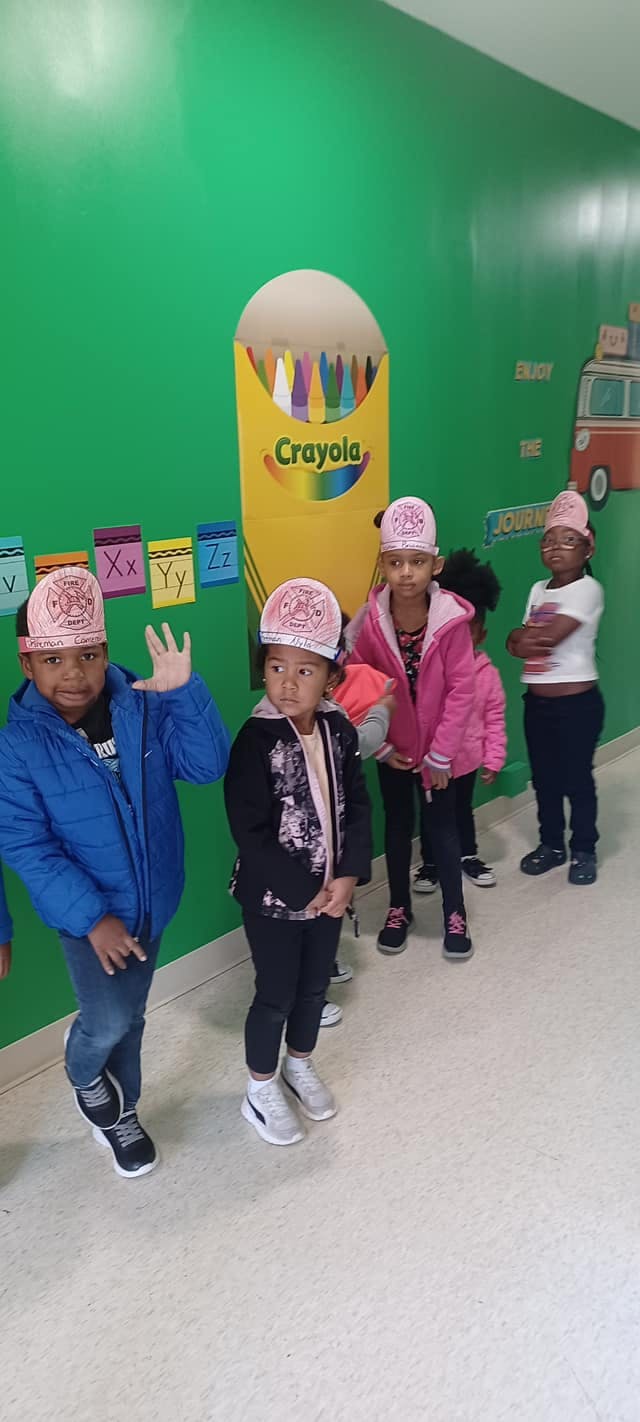 Children standing in a line in a classroom with a large crayon box decoration