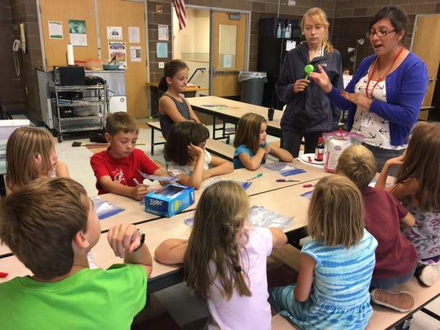 Two adults teaching a group of children in a classroom