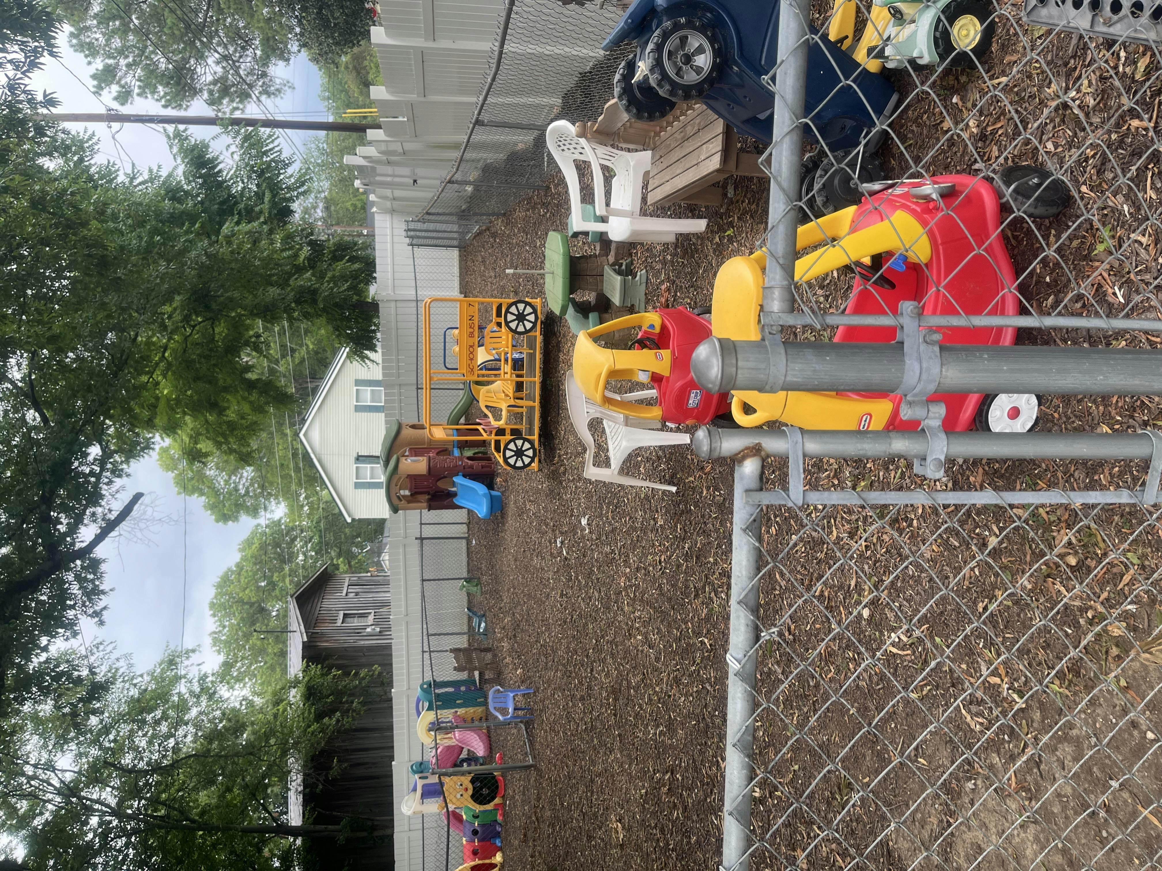 Outdoor play area with various ride-on toys and a chain-link fence