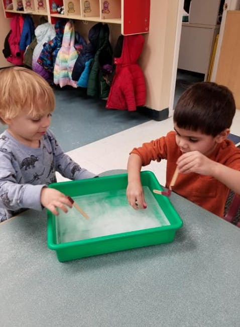 Two children playing with a green tray of soapy water and sticks