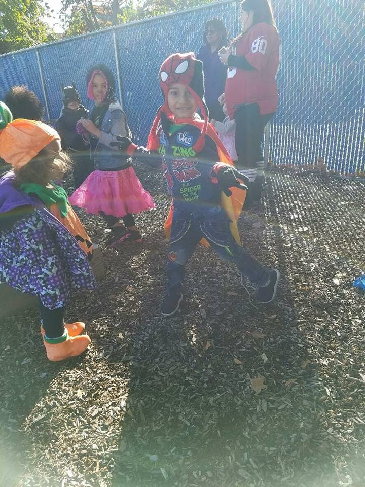 Child in a Spider-Man costume standing outdoors with other children outdoors