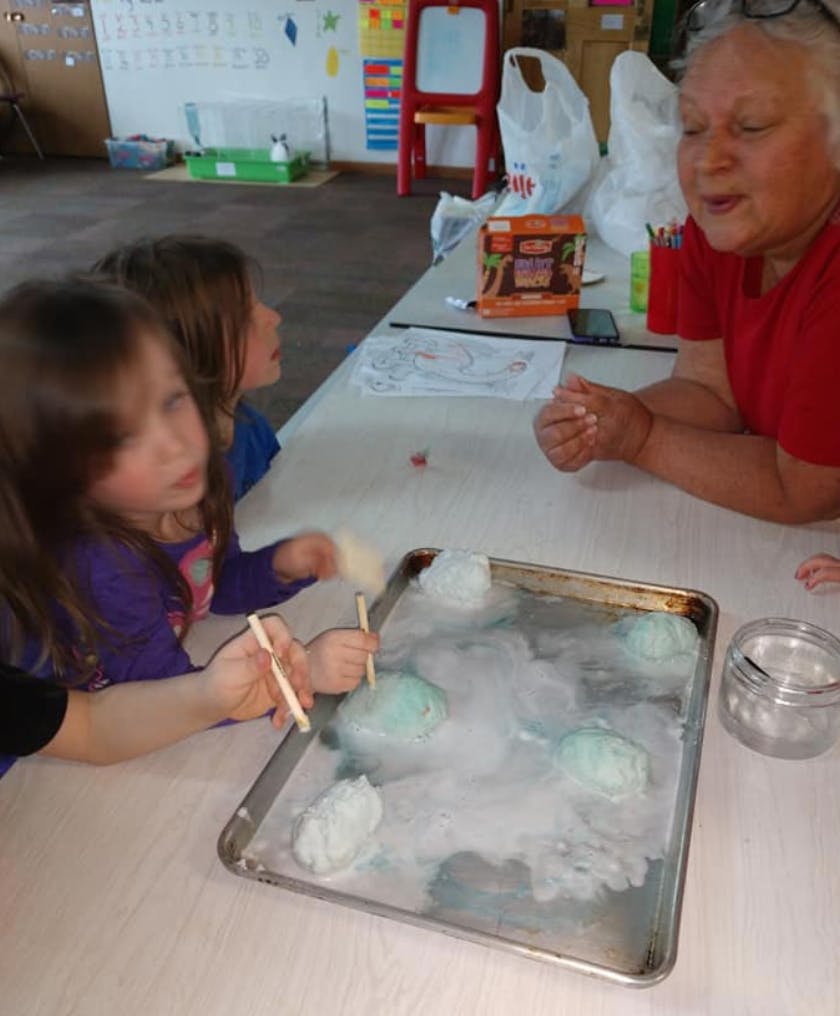 Two children and an adult observing a tray with smoking ice