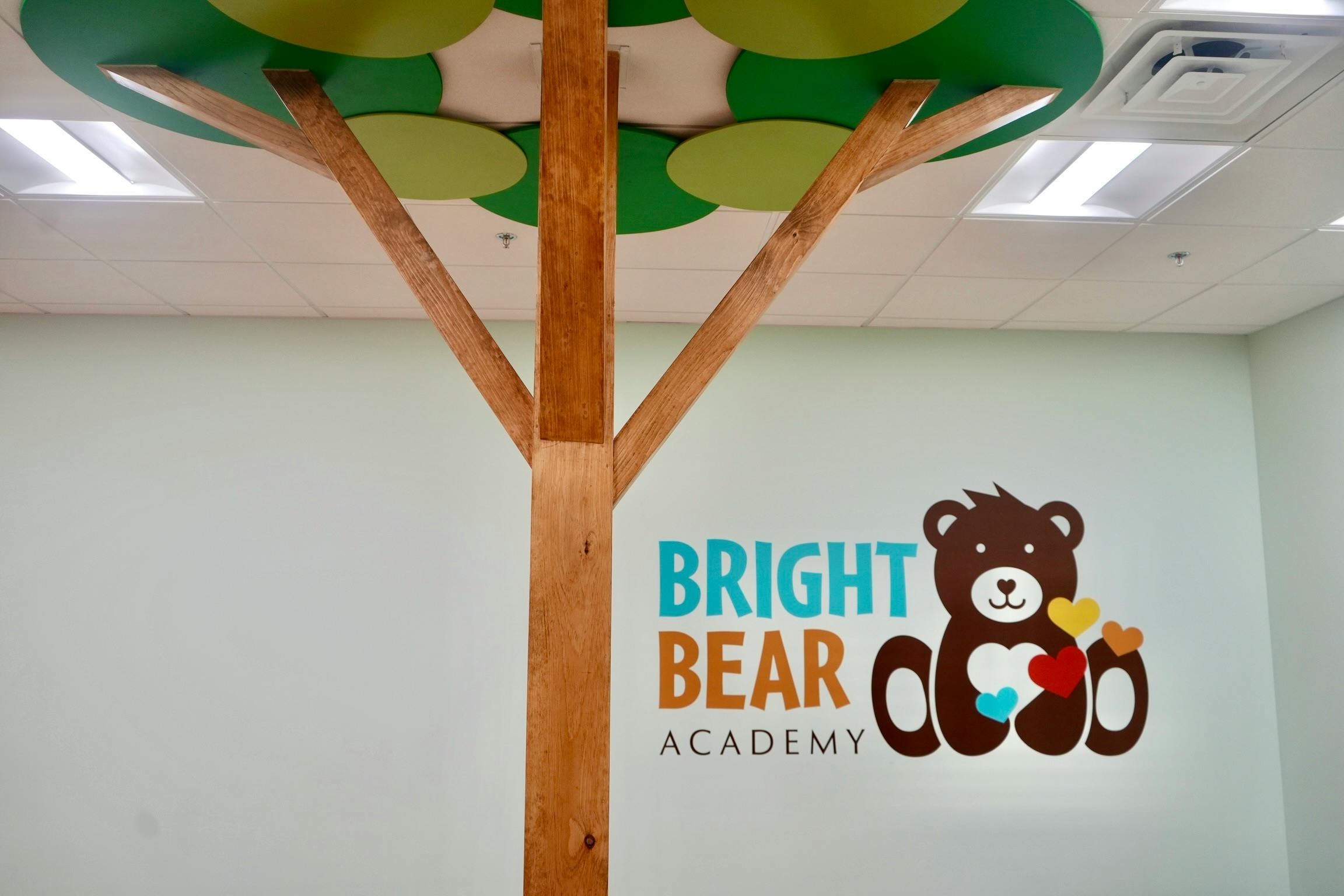 Bright Bear Academy logo with a bear holding hearts next to a wooden tree structure