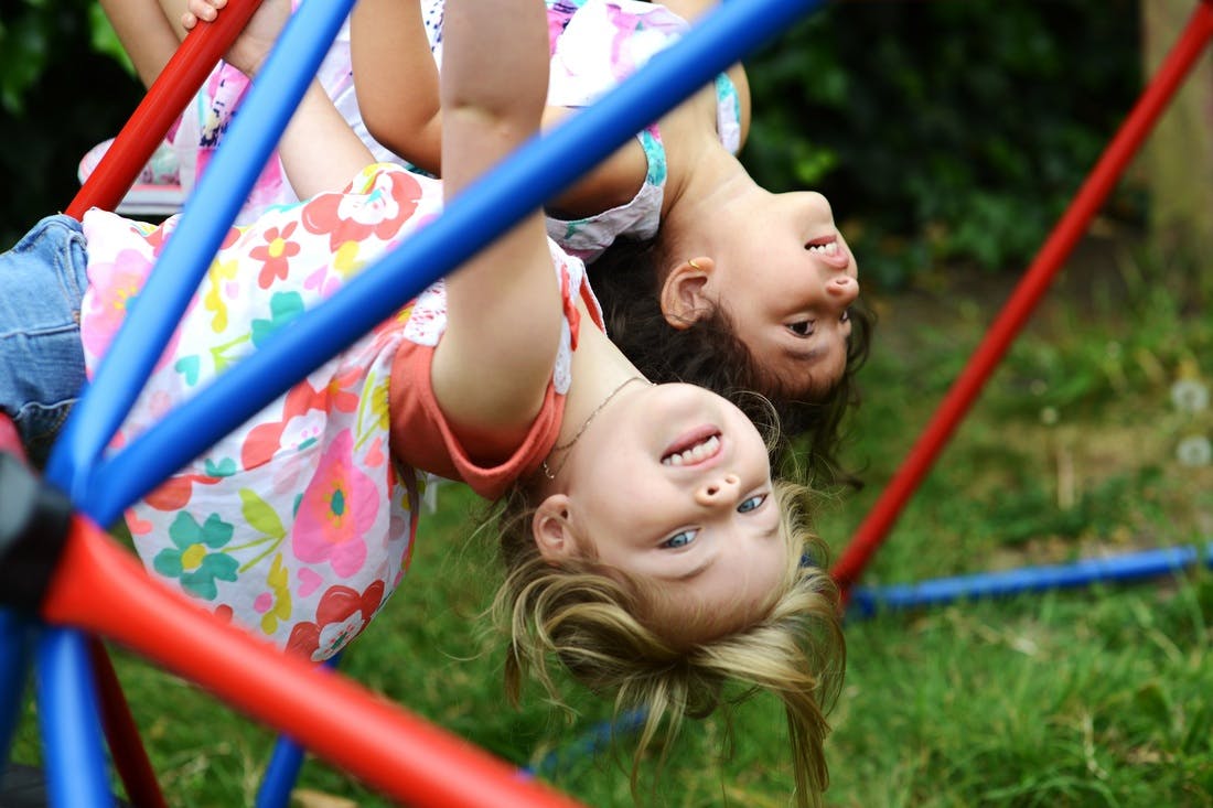 Two children hanging upside down on a jungle gym