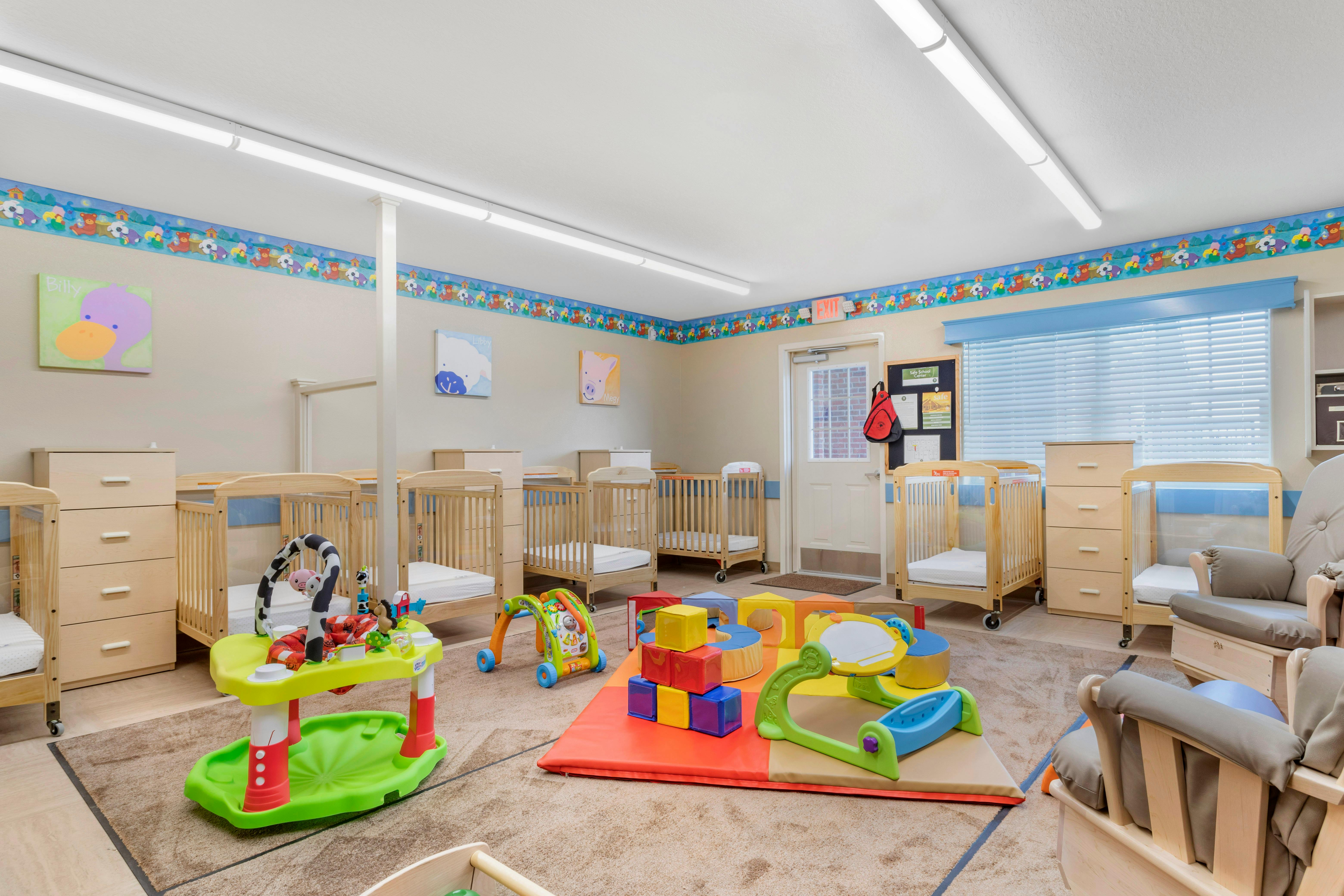 A childcare room with several cribs, dressers, and colorful toys on a play mat