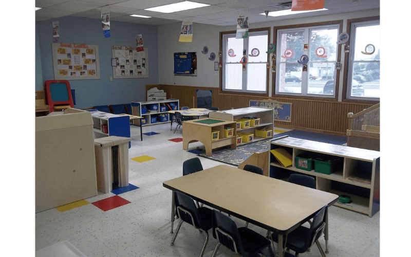 Empty classroom with small tables and chairs, shelves, and colorful items