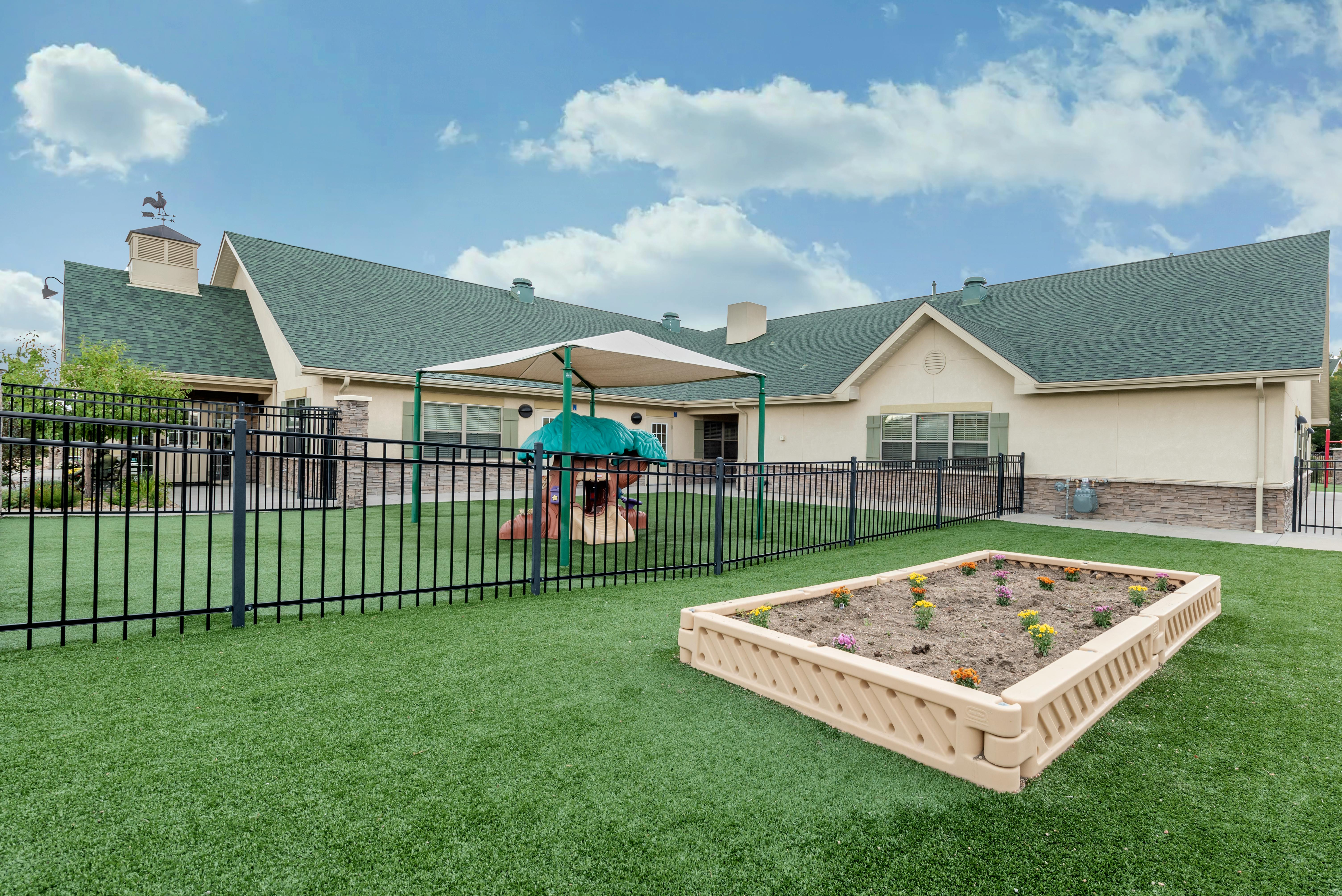 Outdoor playground area with a small play structure, covered awning, and raised garden bed