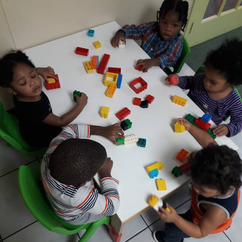 Four children playing with colorful building blocks at a table