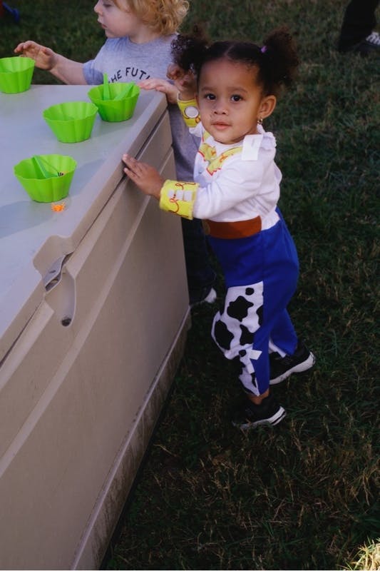 Child wearing a cowboy-themed costume standing by a table with plastic bowls
