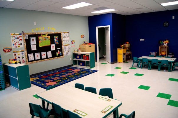 Empty classroom with small tables and chairs, a rug, and a bulletin board