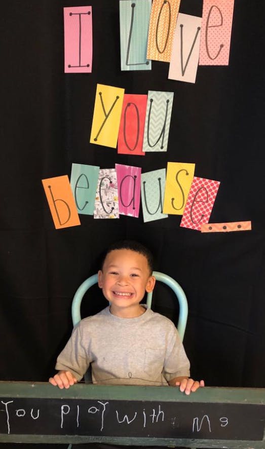 Child sitting in front of a sign that reads "I love you because"