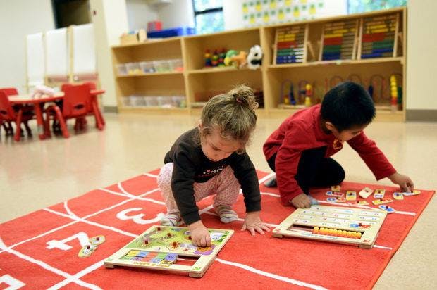 Two children playing with puzzles on a red rug in a classroom