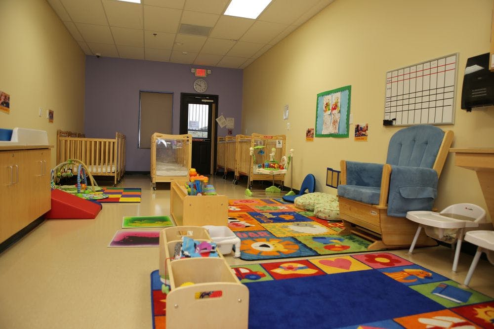 Empty daycare room with cribs, colorful rugs, and play equipment
