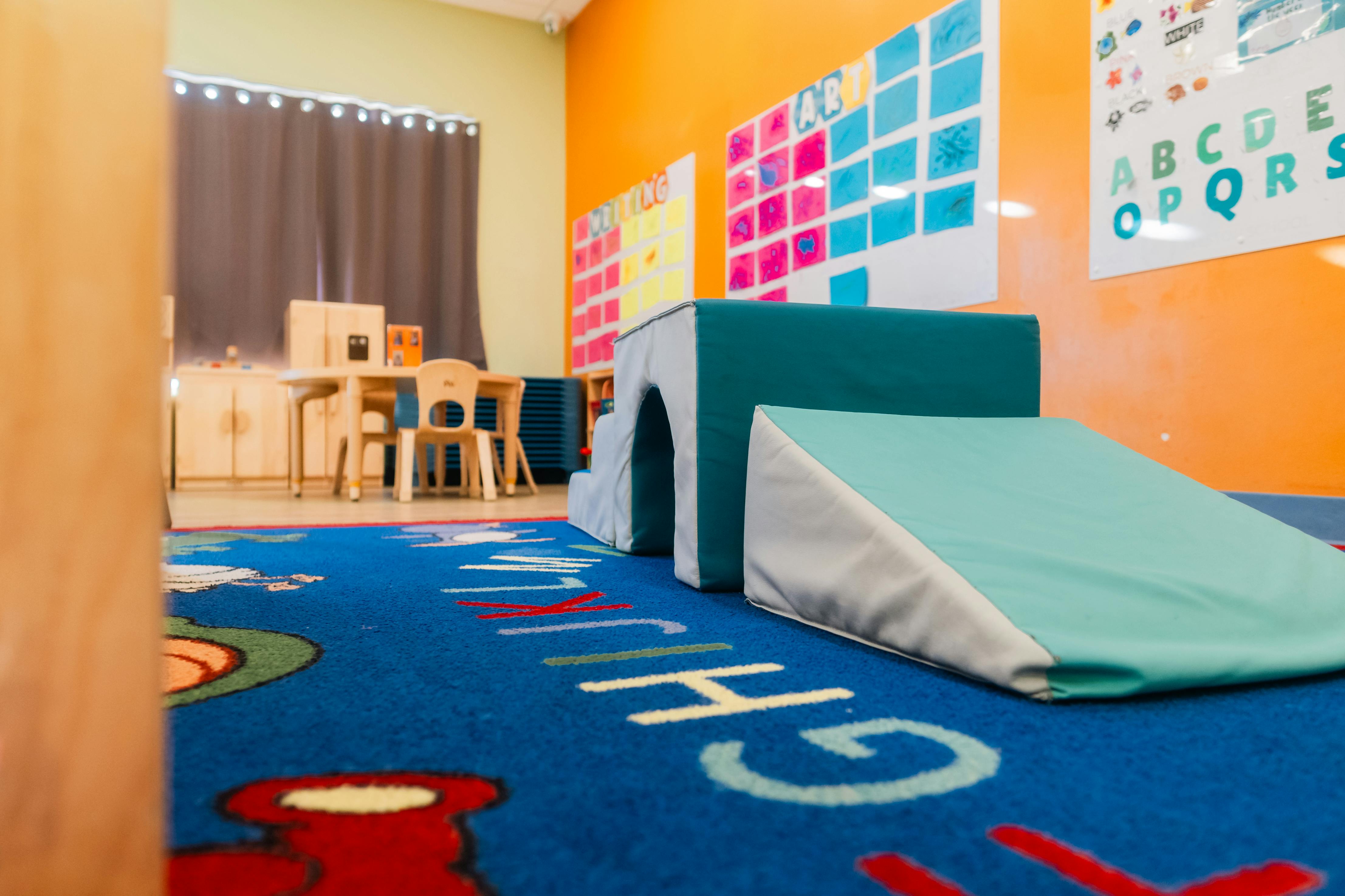 A classroom with a blue alphabet rug and soft play equipment