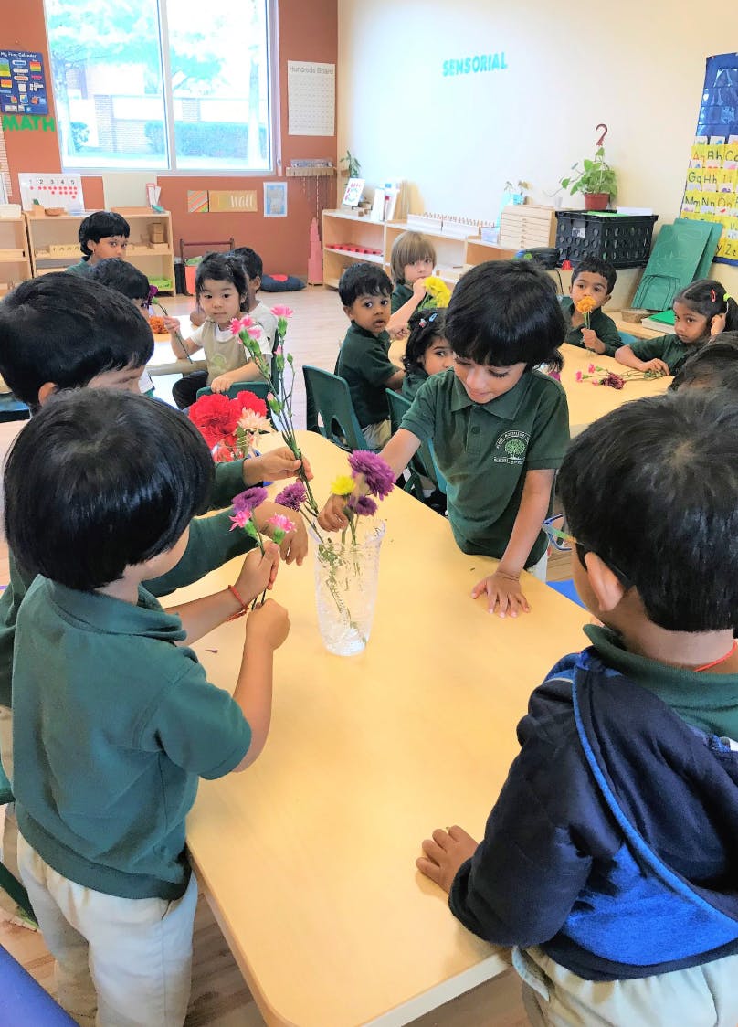 Children arranging flowers in a vase at a table in a classroom