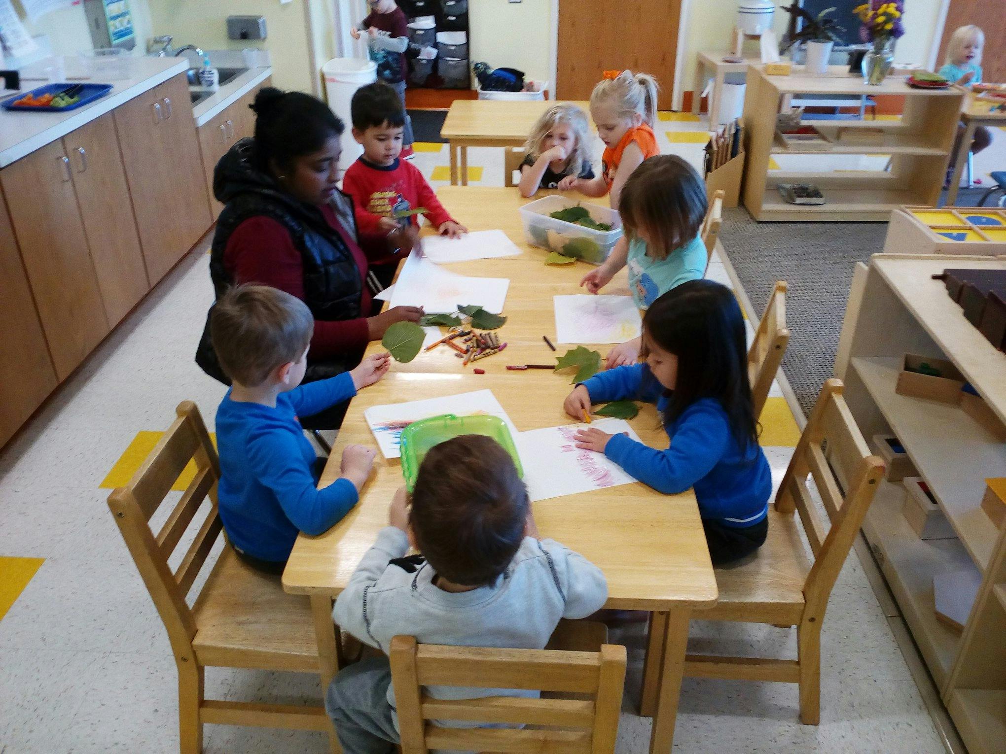 Adult and children at a table with leaves and paper in a classroom