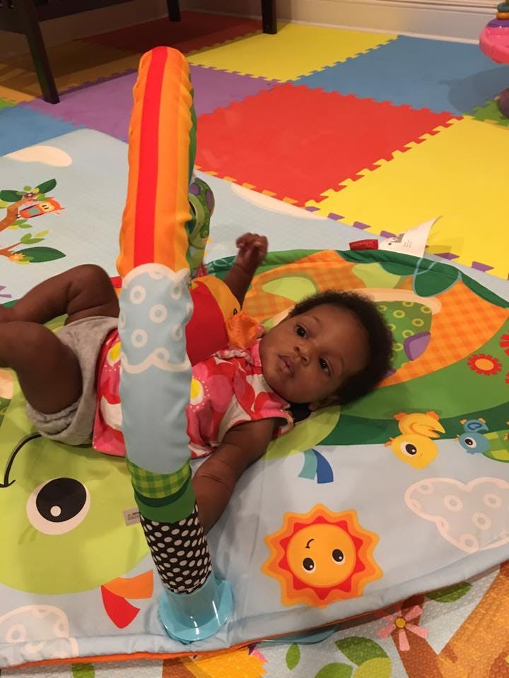 Child lying on a colorful playmat with a toy bar