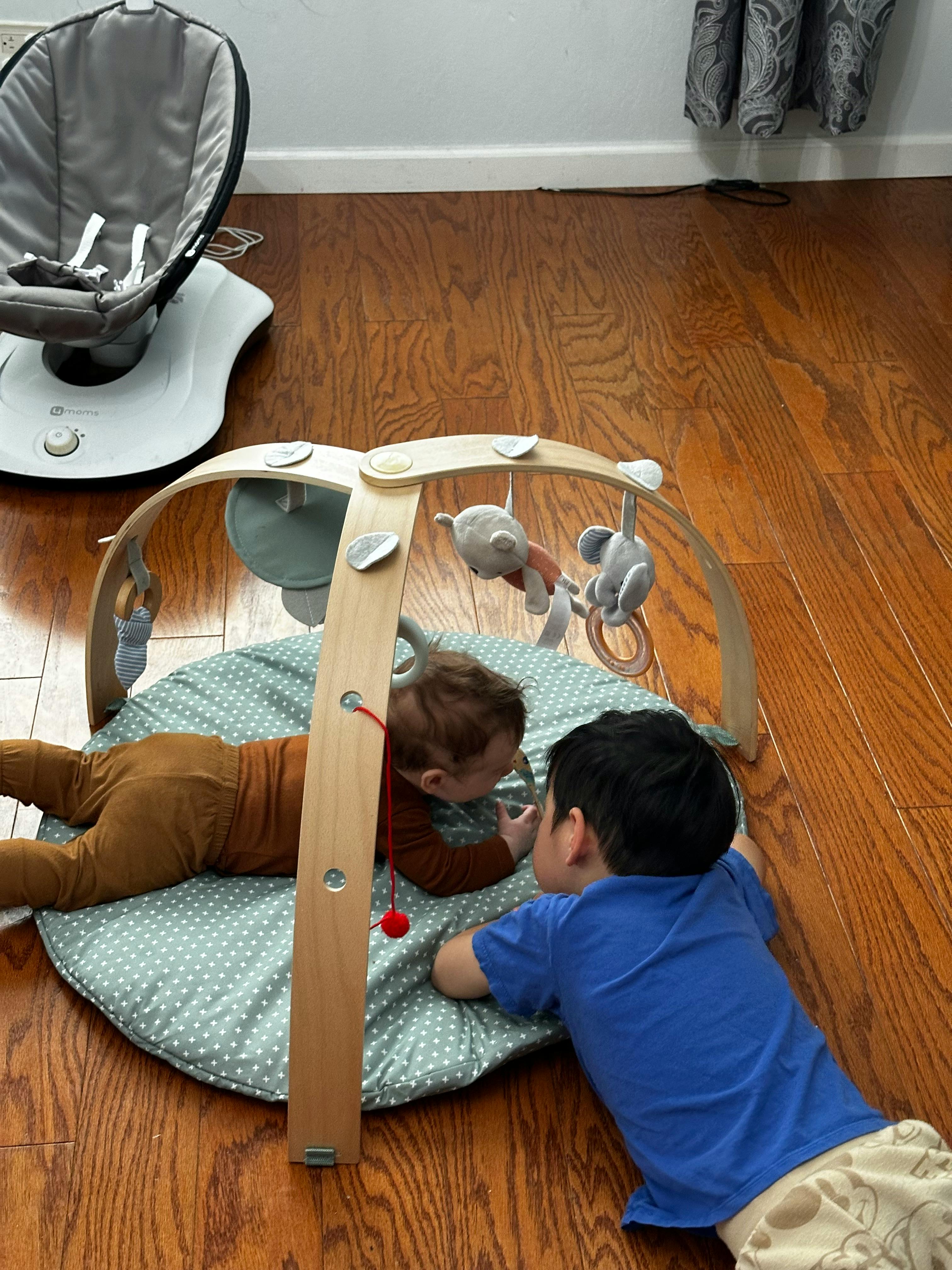 Two children playing on a mat under a wooden play gym