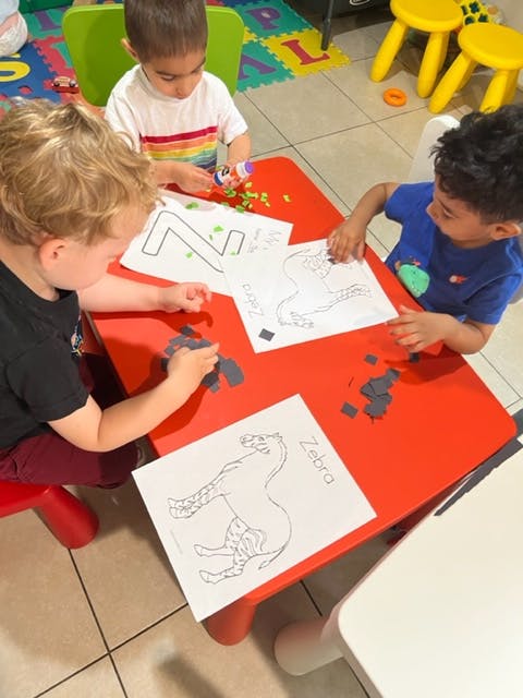 Three children doing crafts at a red table