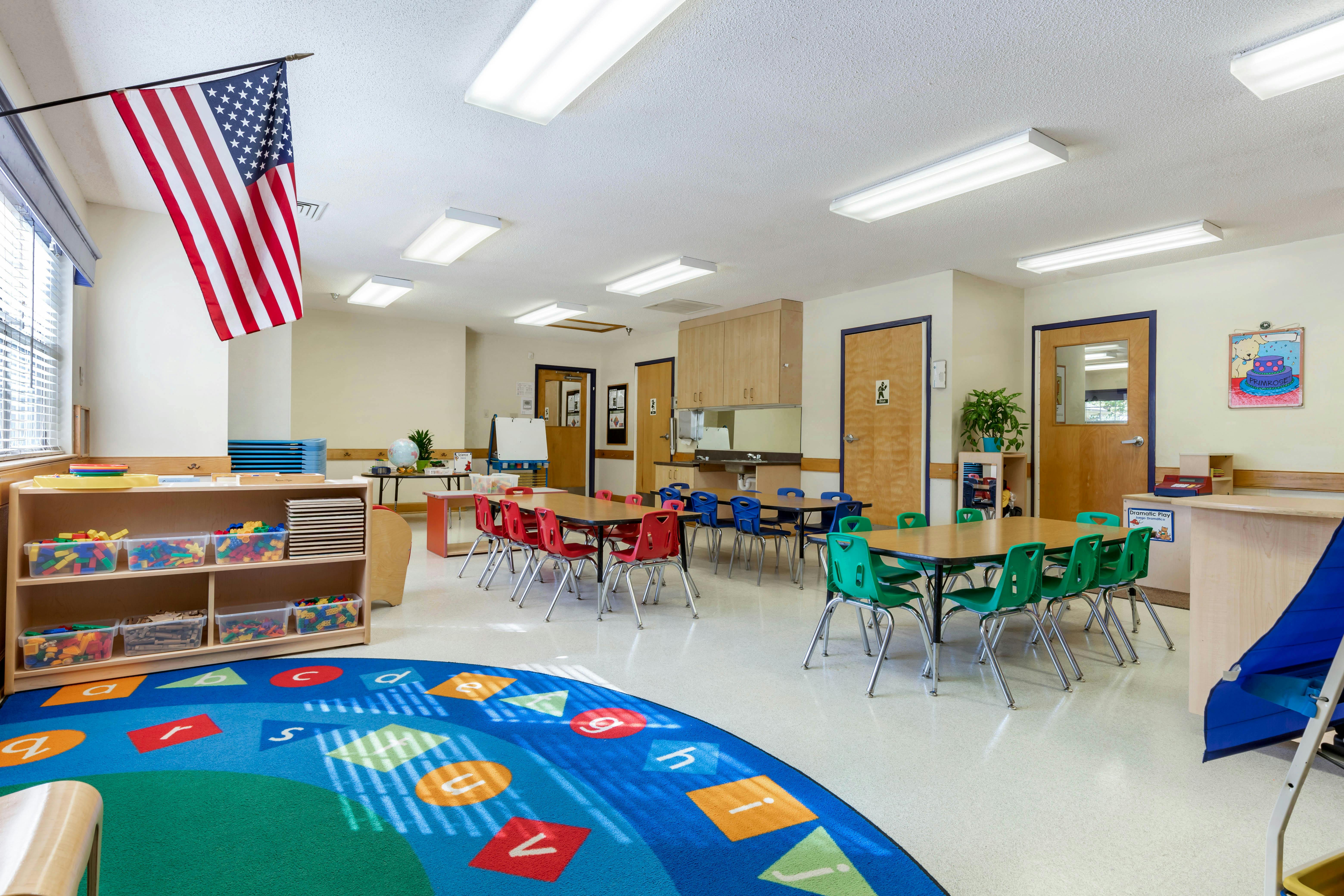 Classroom with small tables and chairs, storage shelves, and an American flag
