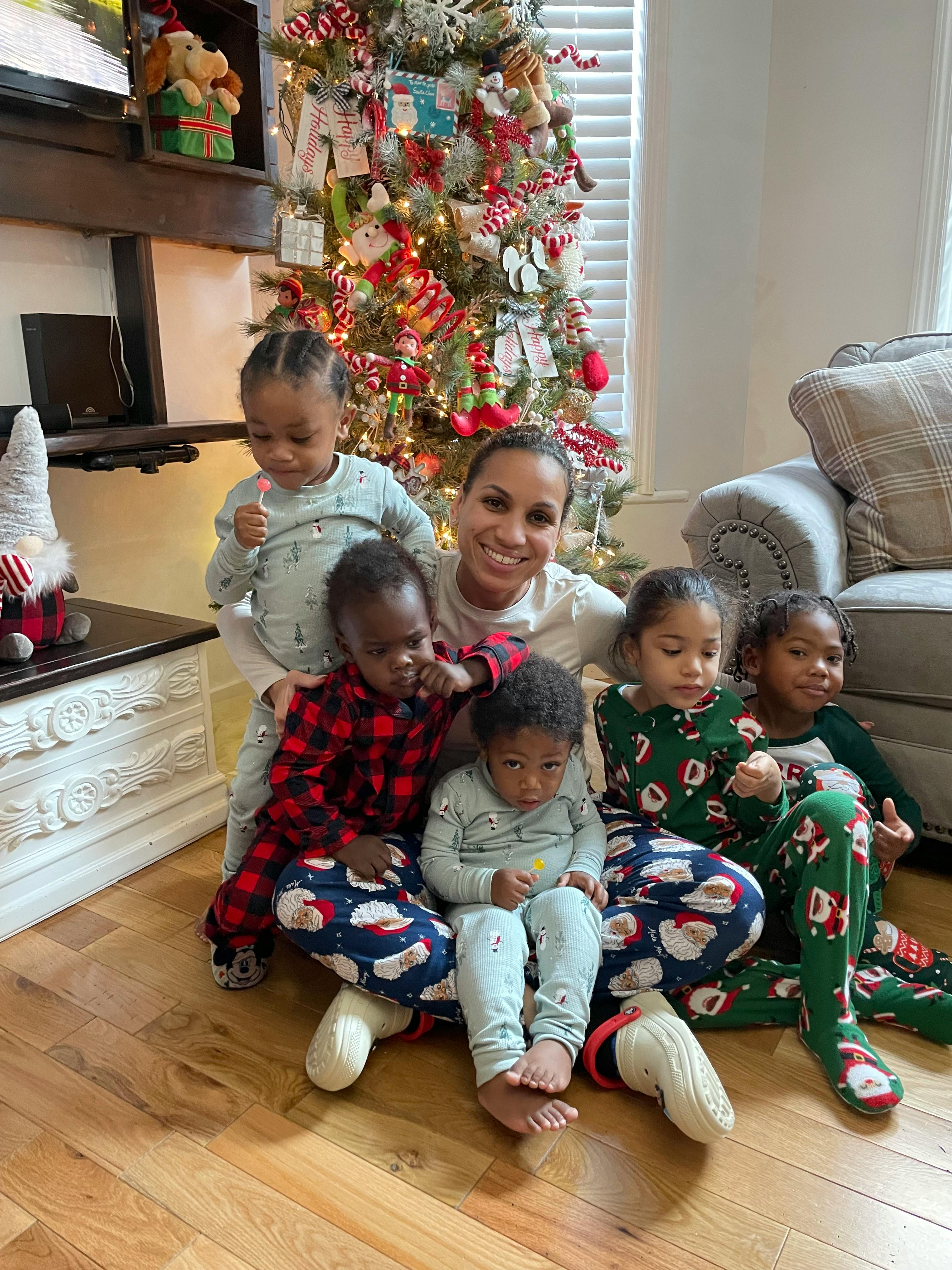 Person with five children in pajamas in front of a Christmas tree