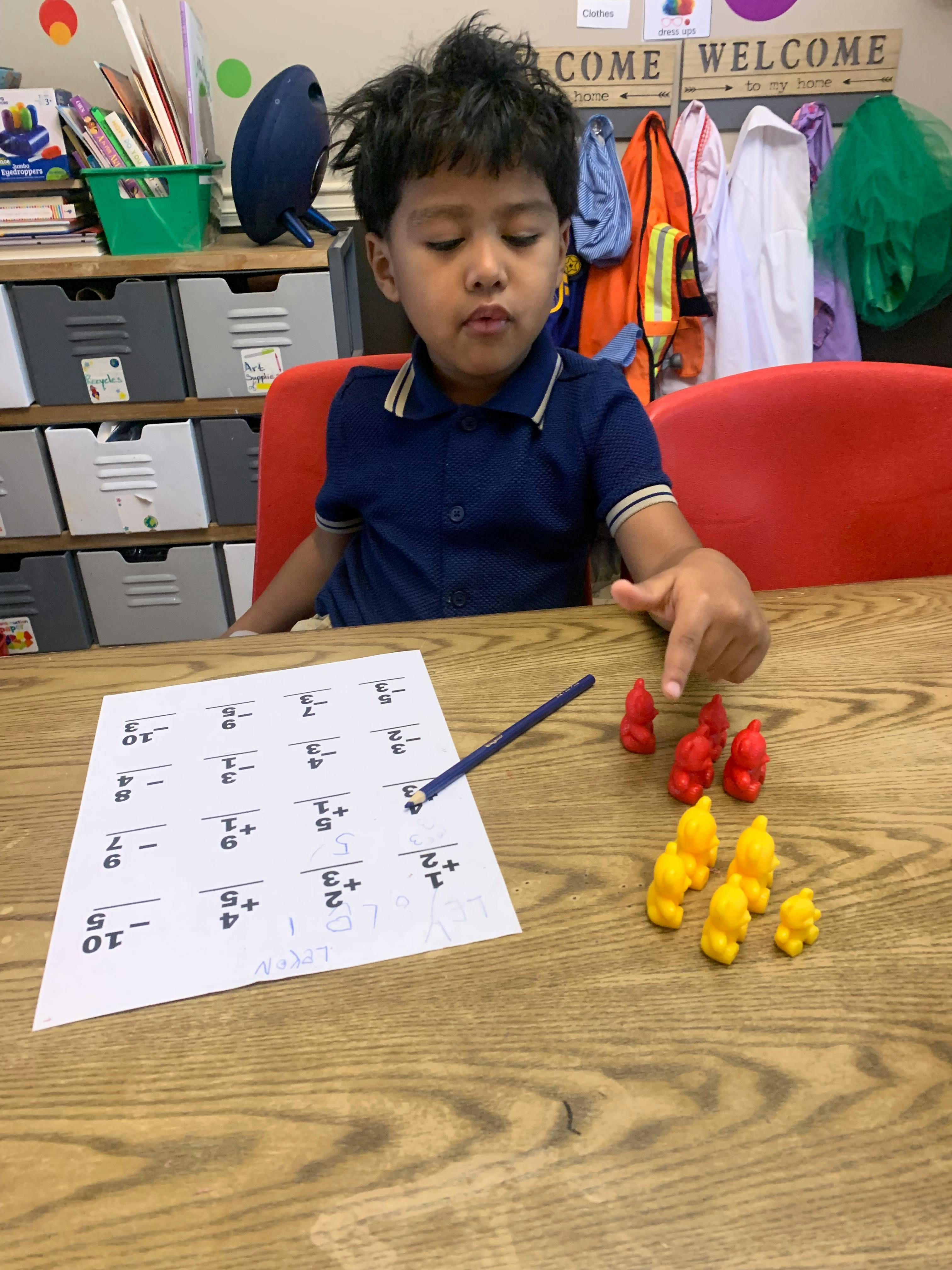Child at a desk, counting with red and yellow bear-shaped manipulatives