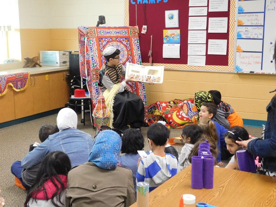Child reading a book to a group of children and adults in a classroom