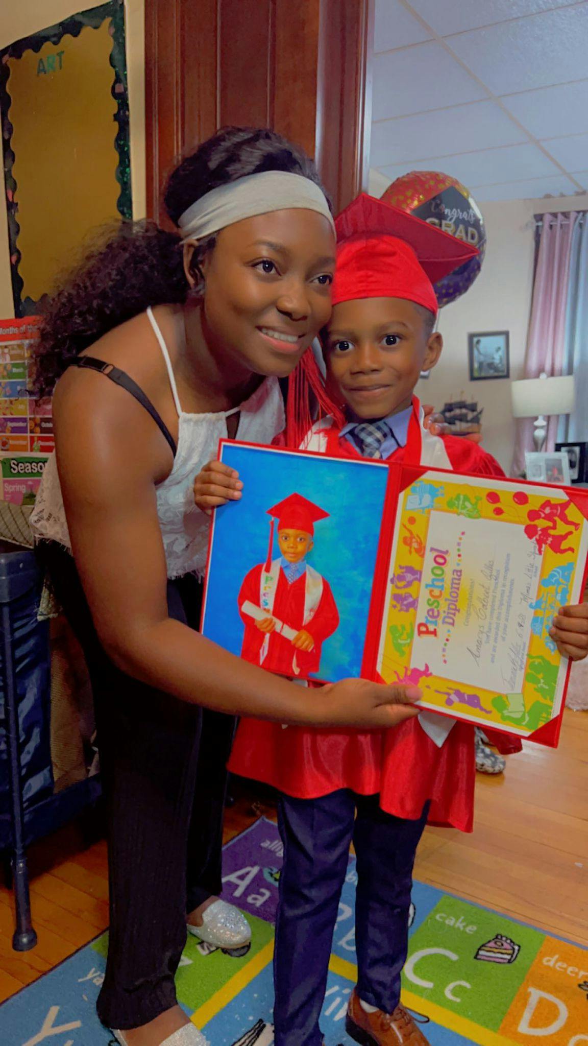 Person and child in graduation attire holding a preschool diploma