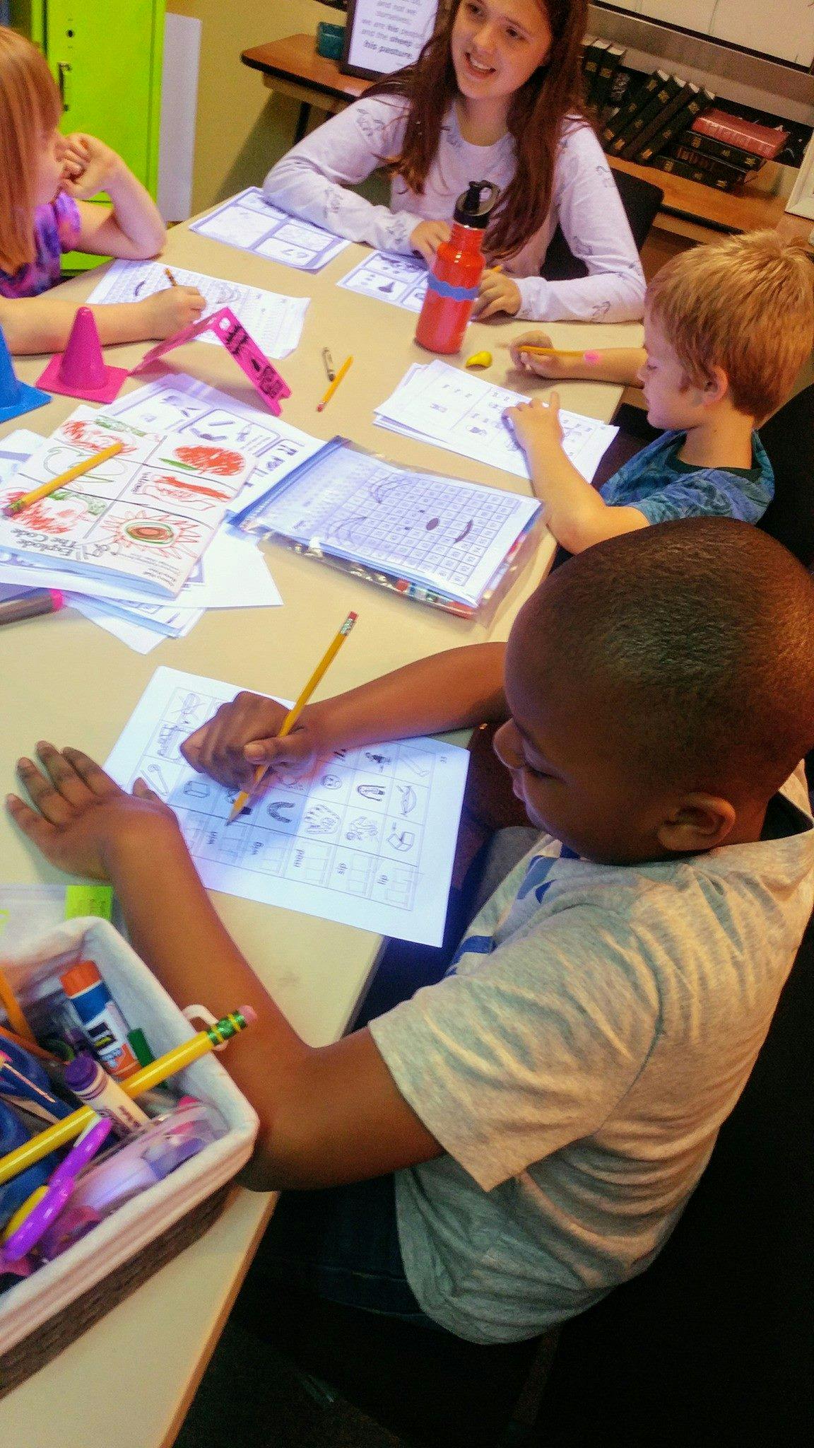 Children drawing and writing at a table in a classroom
