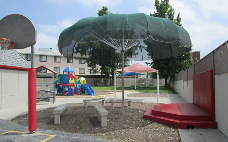 Basketball hoop, green umbrella, and a colorful playground structure