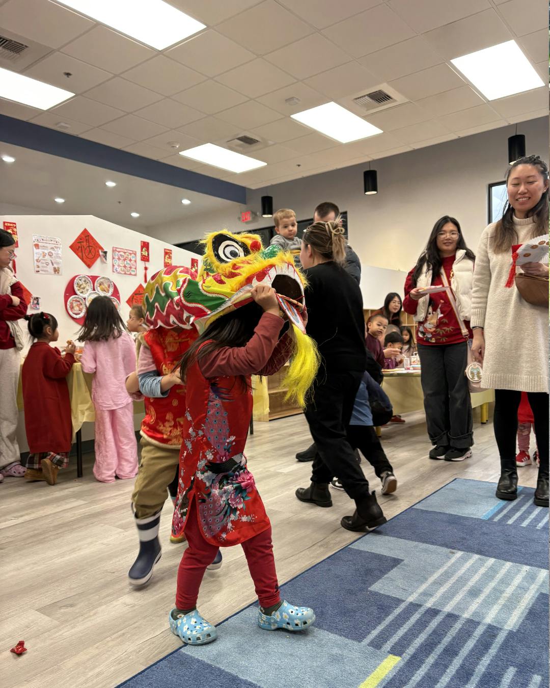 Child wearing a colorful dragon head costume with people in the background