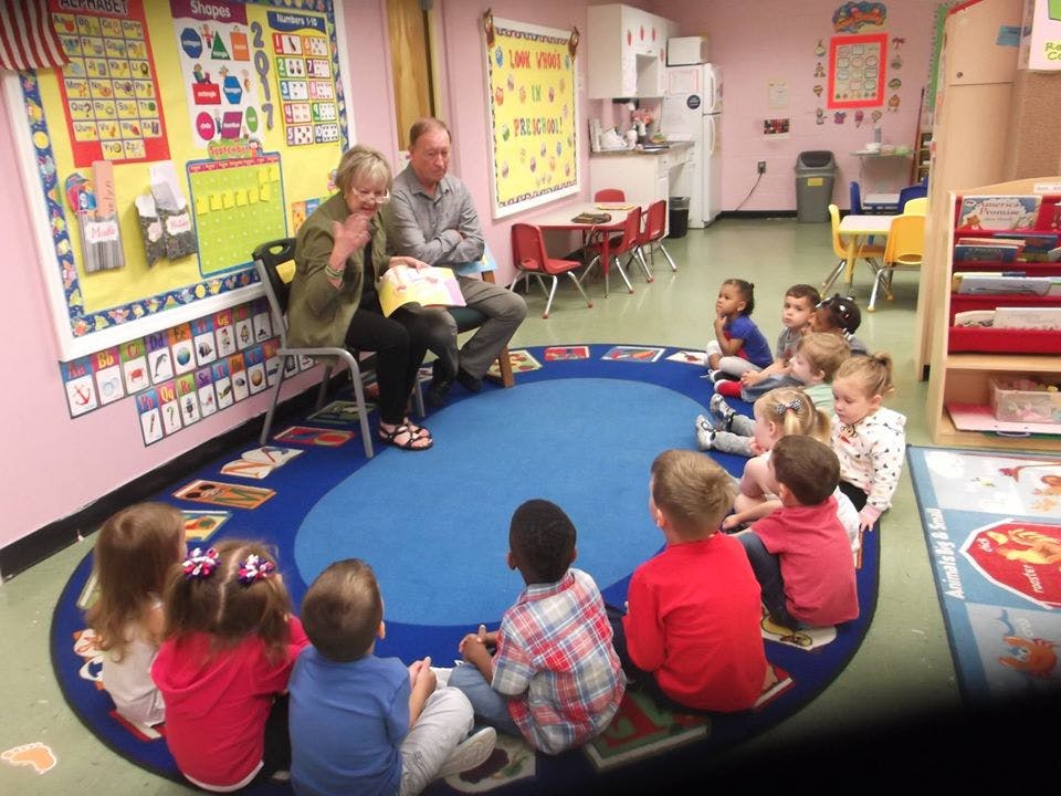 Two adults reading a book to a group of children in a classroom