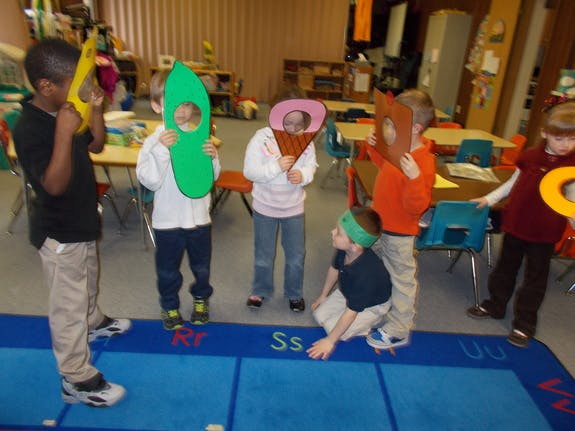 Children holding up large letter cutouts to their faces in a classroom
