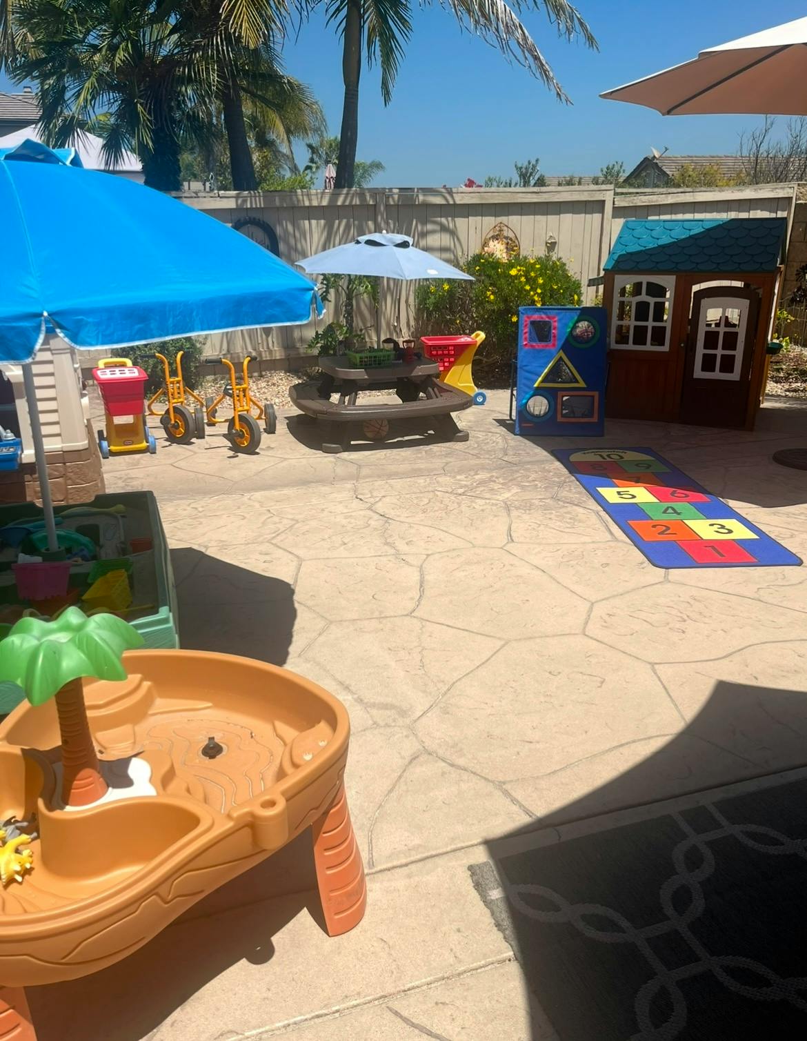 Outdoor play area with various toys, umbrellas, and a small playhouse