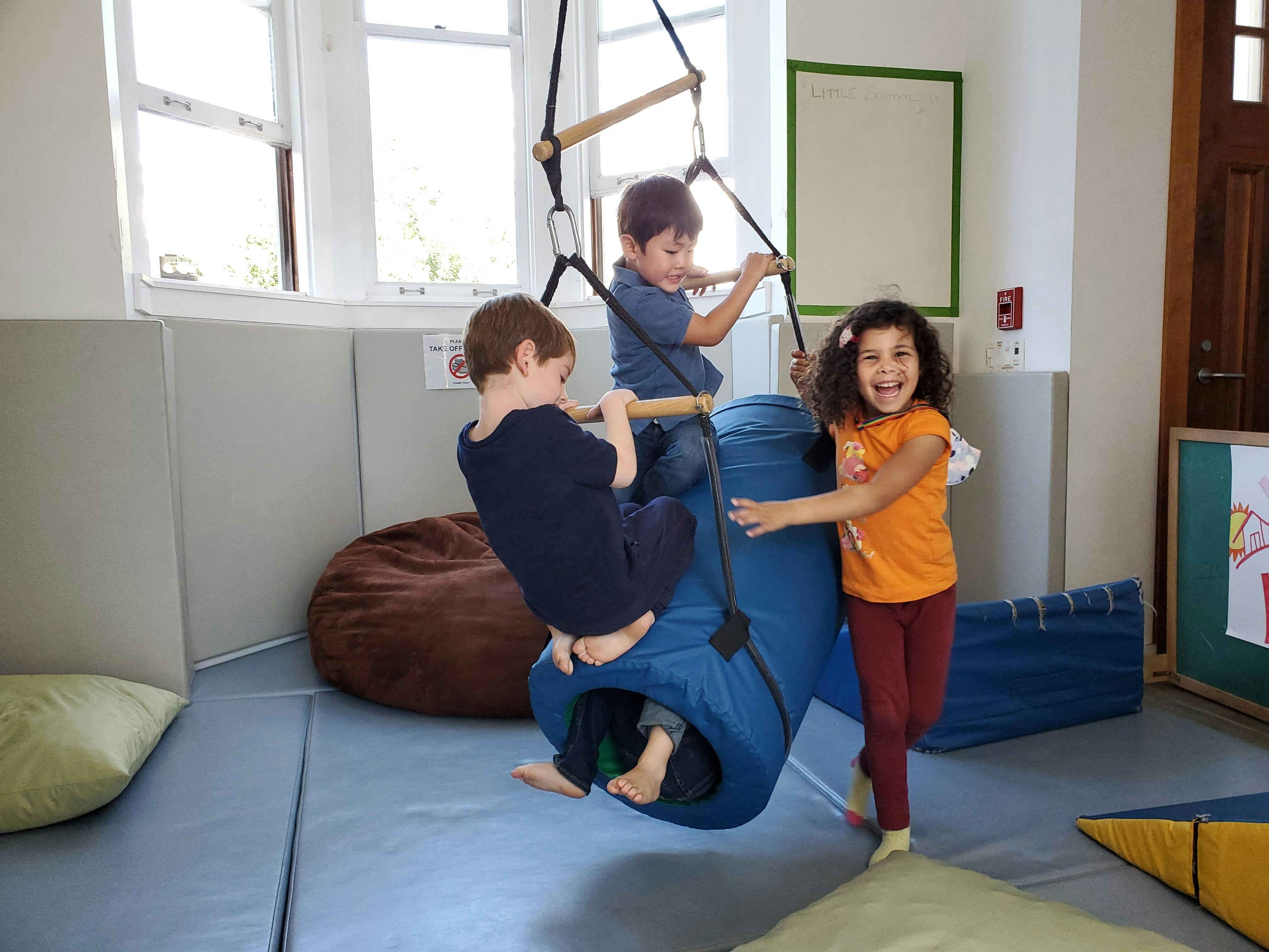 Three children playing on a swing and climbing structure in a room