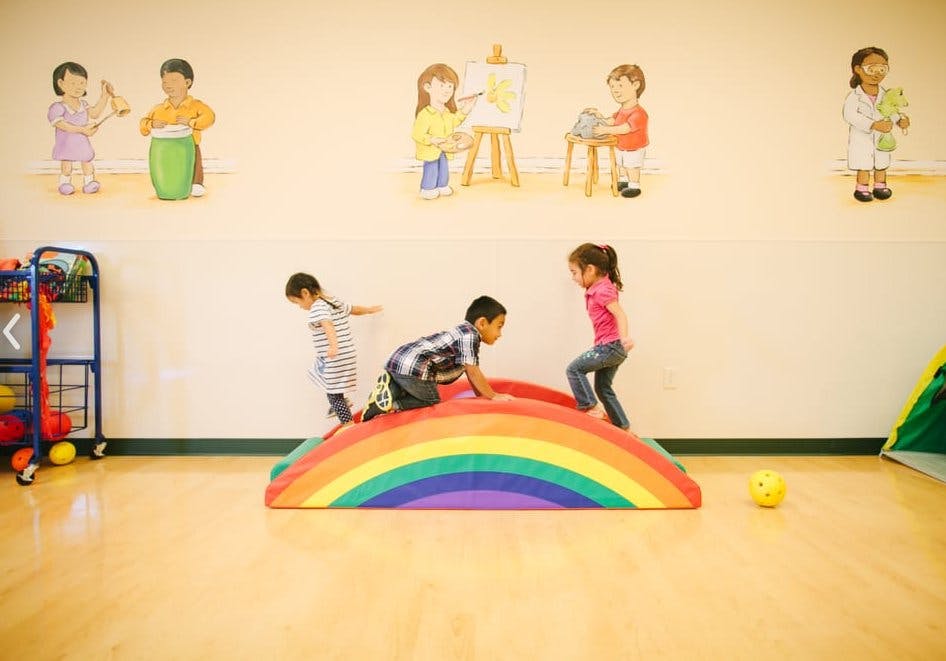 Three children playing on a rainbow-colored climbing toy