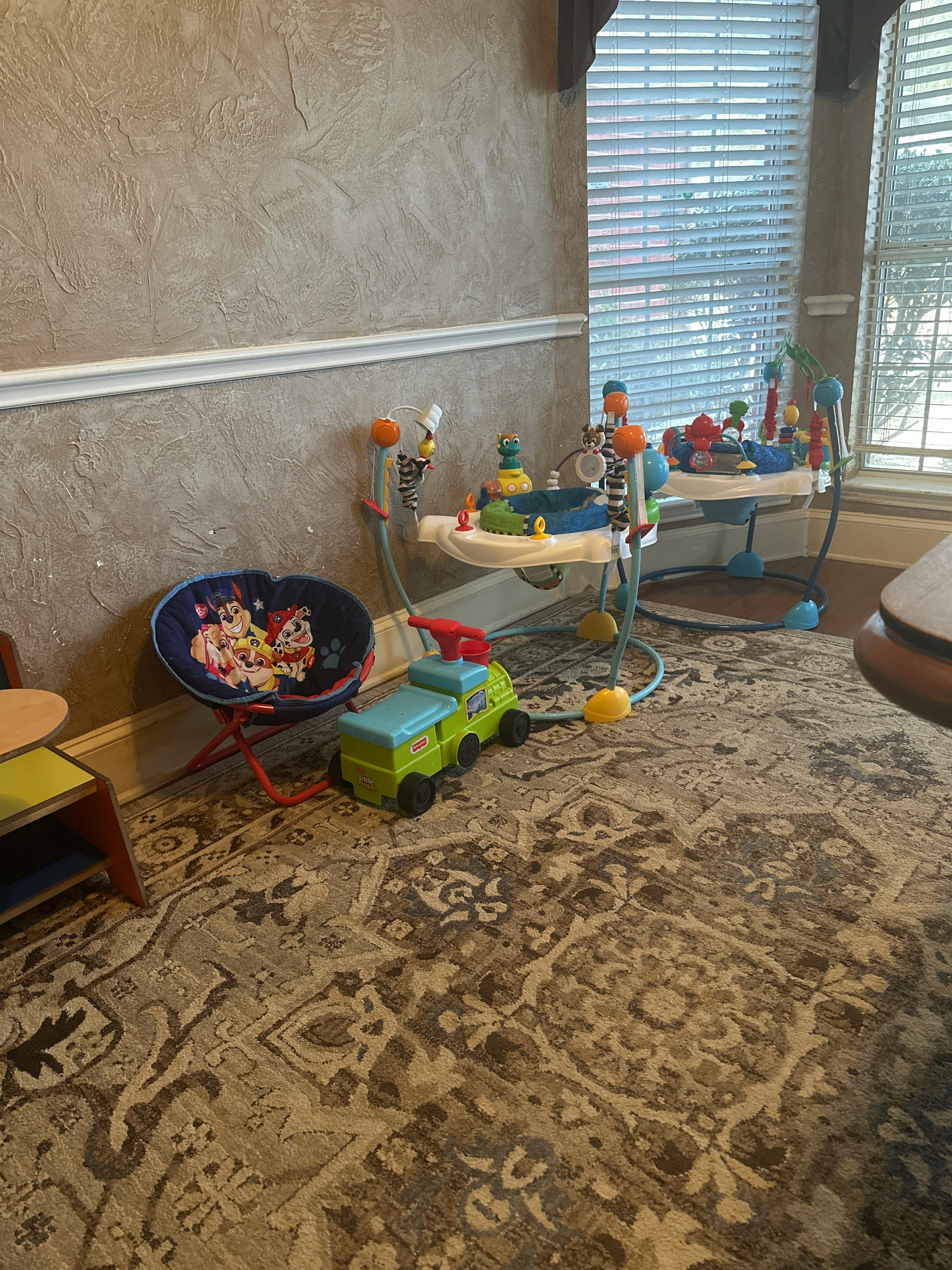 Baby activity center, toy truck, and child's chair on a rug